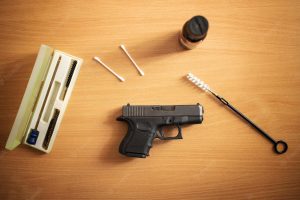 Black handgun beside cleaning supplies on a wooden table