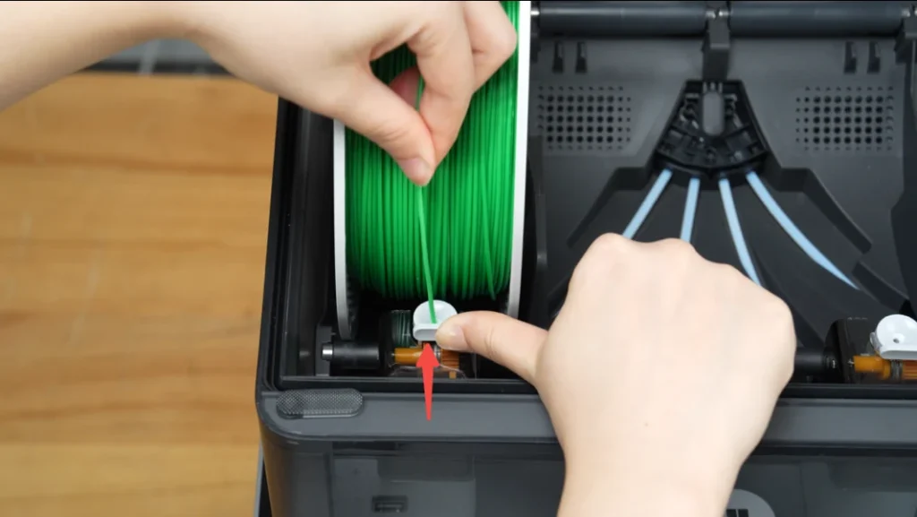 Hands feeding green filament into an AMS 2 Pro spool slot.