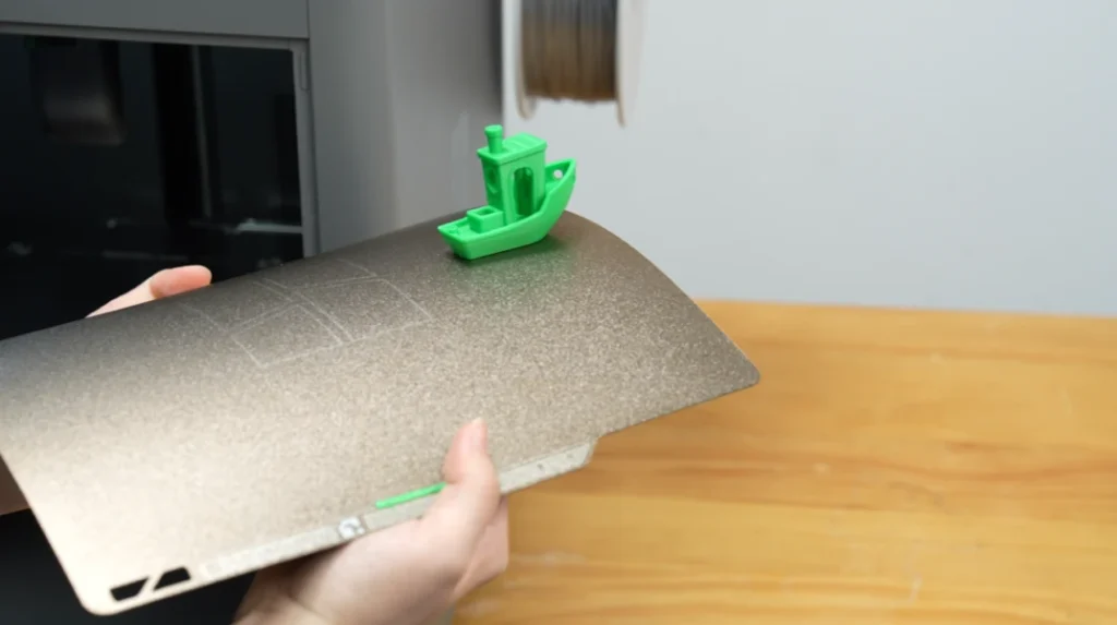 Green Benchy on the P2S textured build plate, held after printing.