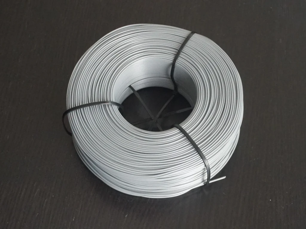 A light gray filament coil secured with black ties on a dark tabletop, without spool flanges.