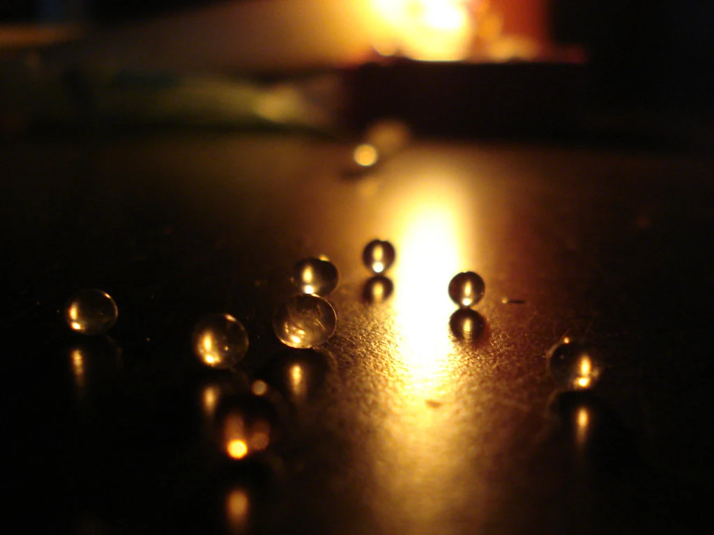 Clear round silica-gel beads scattered on a dark surface with warm light and reflections.