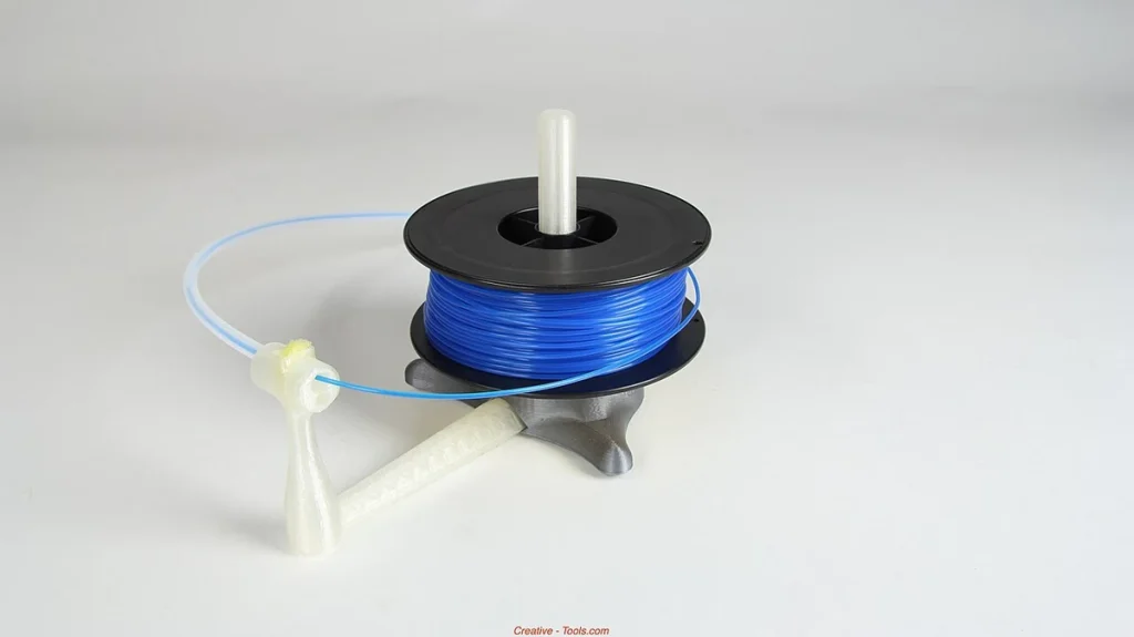 A black spool of blue filament on a gray and translucent printed stand, with filament passing through a guide arm.