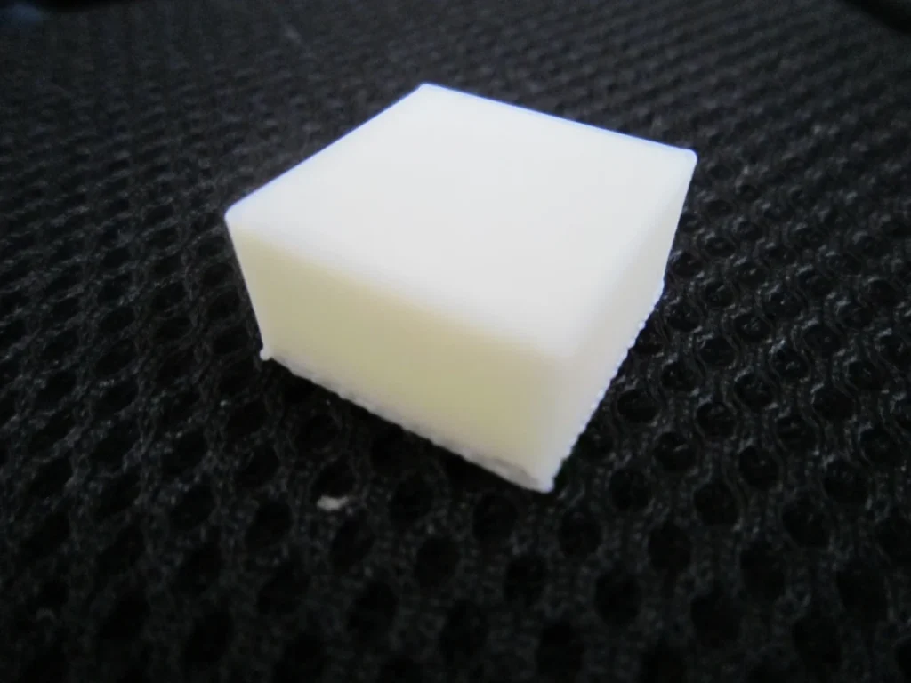 Small white printed cube with uneven lower edges resting on dark textured fabric.