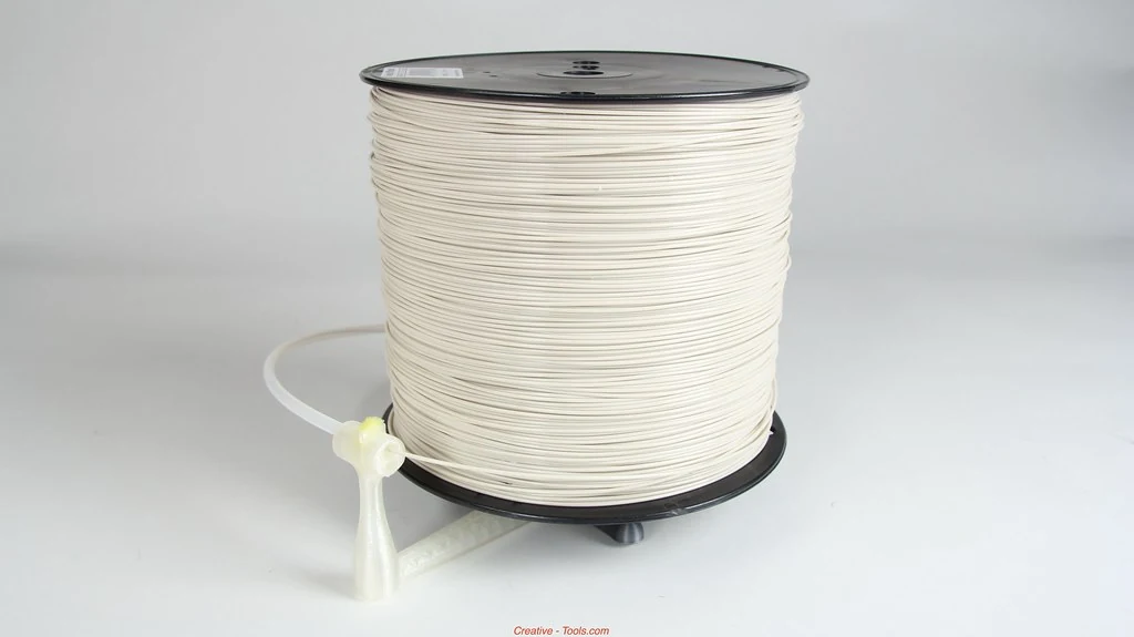 White filament is wound on a black spool mounted horizontally on a translucent printed holder with a guide tube.