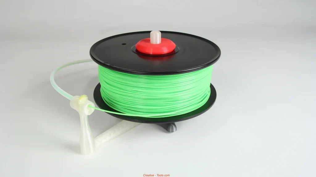 Green filament on a black spool mounted horizontally on a printed stand, with a red center collar and filament passing through a guide.