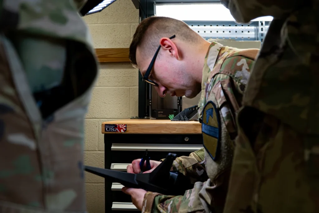 A uniformed technician holds a black printed aircraft frame and blue-handled cutters at a workshop bench.