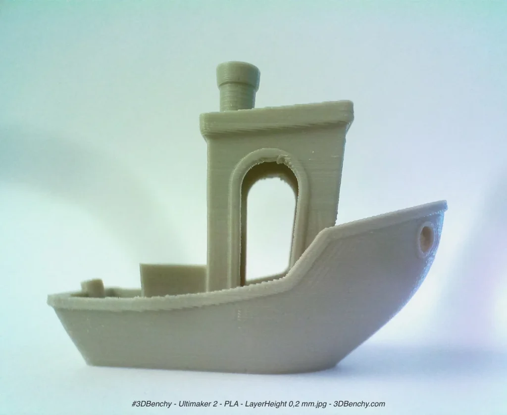 A pale 3D-printed Benchy boat with visible horizontal layers, an arched cabin doorway and a chimney against a light background.