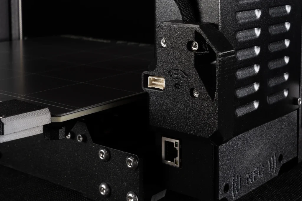 Close-up of a Prusa MK4S electronics housing beside the bed, with an Ethernet socket and wireless-symbol cover.