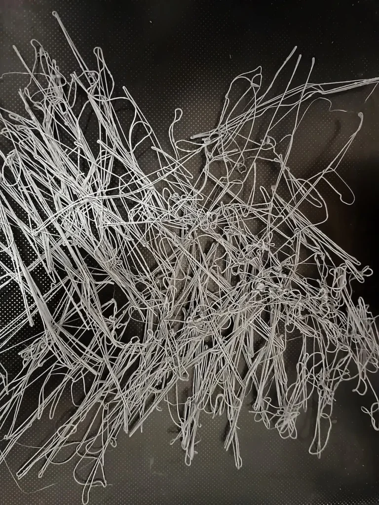 Tangled white extruded strands lie across a dark dotted printer build surface.