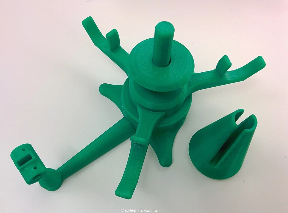 Green printed spool-holder components rest on a white surface, with an upright spindle and separate conical piece.
