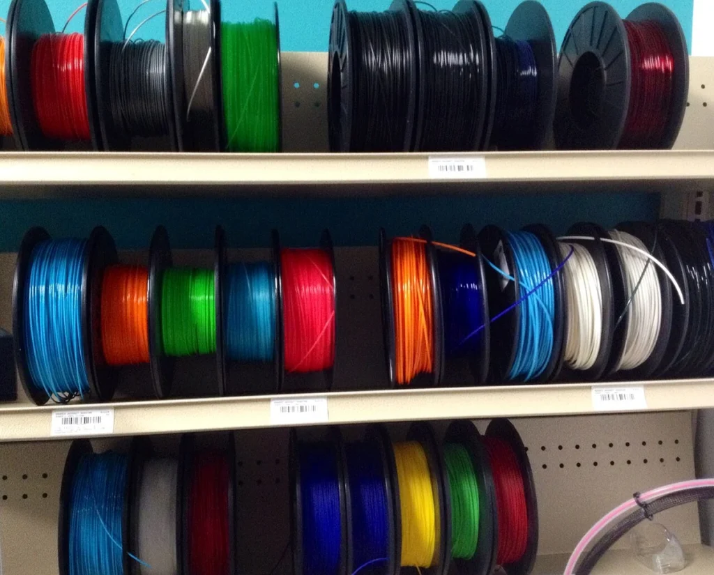 Multiple colored filament spools stand upright on three open shelves.